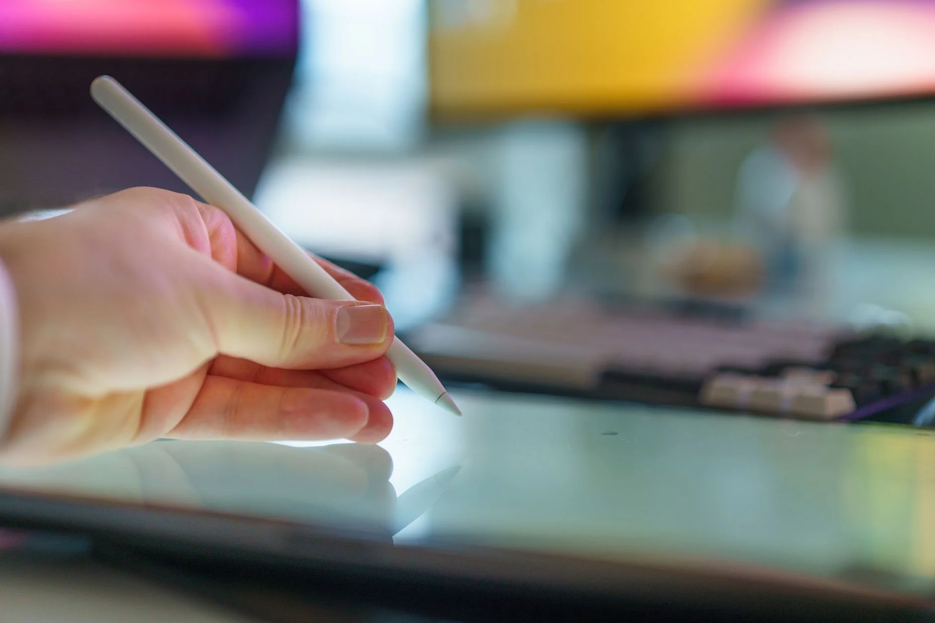 A designer's hand sketching wireframe boxes on a tablet next to a notebook of UI annotations